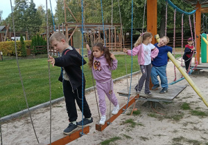 Dzieci idą po równoważni z desek zawieszonej nad ziemią