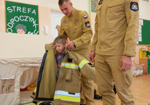 Chłopiec zakłada kurtkę strażacką.
