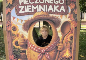 Chłopiec pozuje do pamiątkowego zdjęcia w jesiennej fotobudce przedstawiającej wesołego ziemniaka.