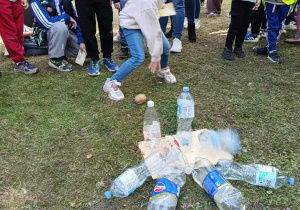 Dziewczynka rzuca ziemniakiem w kierunku plastikowych butelek podczas konkurencji zręcznościowej na pikniku.