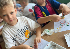 Dwóch chłopców wykonuje prace plastyczne z motywem jesiennego drzewa, używając papierowych rolek i kolorowych farb.