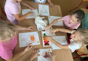 Dzieci zgromadzone przy stoliku tworzą prace plastyczne o tematyce jesiennej, korzystając z farb i papierowych rolek.