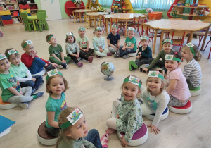 Przedszkolaki ubrane na zielono siedzą w kręgu.