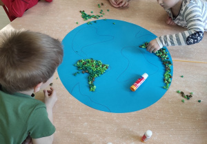 Przedszkolaki wyklejają zieloną krepiną kontury kontynentów.