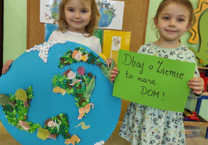Dziewczynki prezentują wykonaną pracę plastyczną i hasło: Dbaj o Ziemię - to nasz dom.