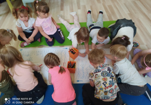 Dzieci kolorują obrazek łąki na dużym kartonie