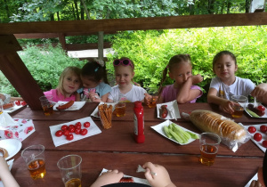 Dzieci jedzą upieczone kiełbaski nad ogniskiem