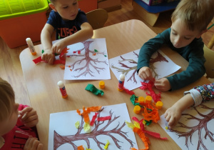 Dzieci wykonują pracę plastyczną "Drzewo", przyklejają listki wykonane z bibuły na gałązkach drzewa