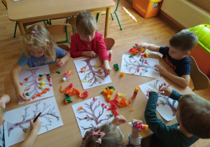 Dzieci wykonują pracę plastyczną "Drzewo", przyklejają listki wykonane z bibuły na gałązkach drzewa