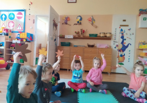 Dzieci siedzą na macie i uczestniczą w zabawie naśladowczej "Wieje wiatr" z wykorzystaniem sylwet listków