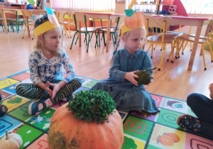 Dzieci siedząc na dywanie podają sobie dynię i poznają jej kształt i strukturę