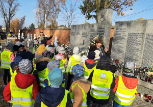Dzieci stoją przy pomniku i słuchają opowieści o historii.