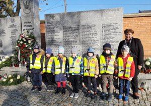 Dzieci z grupy III wraz z Panią stoją przy pomniku poległych żołnierzy.