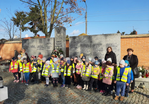 Dzieci z grupy I, II, III wraz z Paniami stoją przy pomniku poległych żołnierzy.