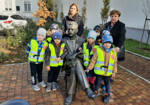 Dzieci z grupy III wraz z Panią pozują przy pomniku znajdującym się przy Urzędzie Stanu Cywilnego .