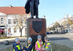 Cztery dziewczynki trzymają znicze przed pomnikiem Józefa Piłsudskiego.