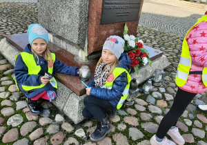 Dwie dziewczynki kucają przy pomniku Józefa Piłsudskiego.