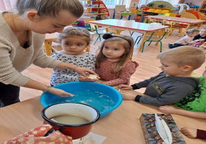 Dzieci przelewają wosk z pomocą nauczyciela