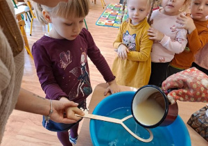 Dziewczynka przelewa wosk z pomocą nauczyciela