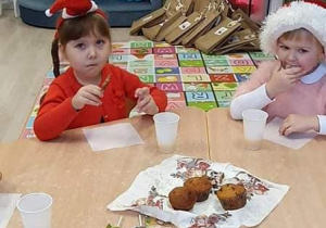 dzieci w czapkach Mikołaja jedzą słodki poczęstunek