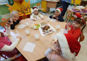 dzieci w czapkach Mikołaja jedzą słodki poczęstunek