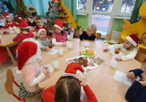 dzieci w czapkach Mikołaja jedzą słodki poczęstunek