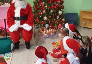 dzieci w czapkach Mikołaja siedzą na macie przed Świętym Mikołajem