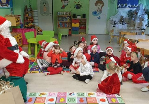 dzieci w czapkach Mikołaja siedzą na macie przed Świętym Mikołajem