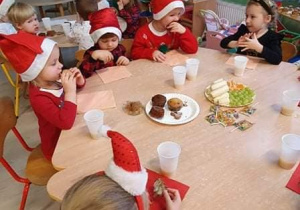 dzieci w czapkach Mikołaja jedzą słodki poczęstunek
